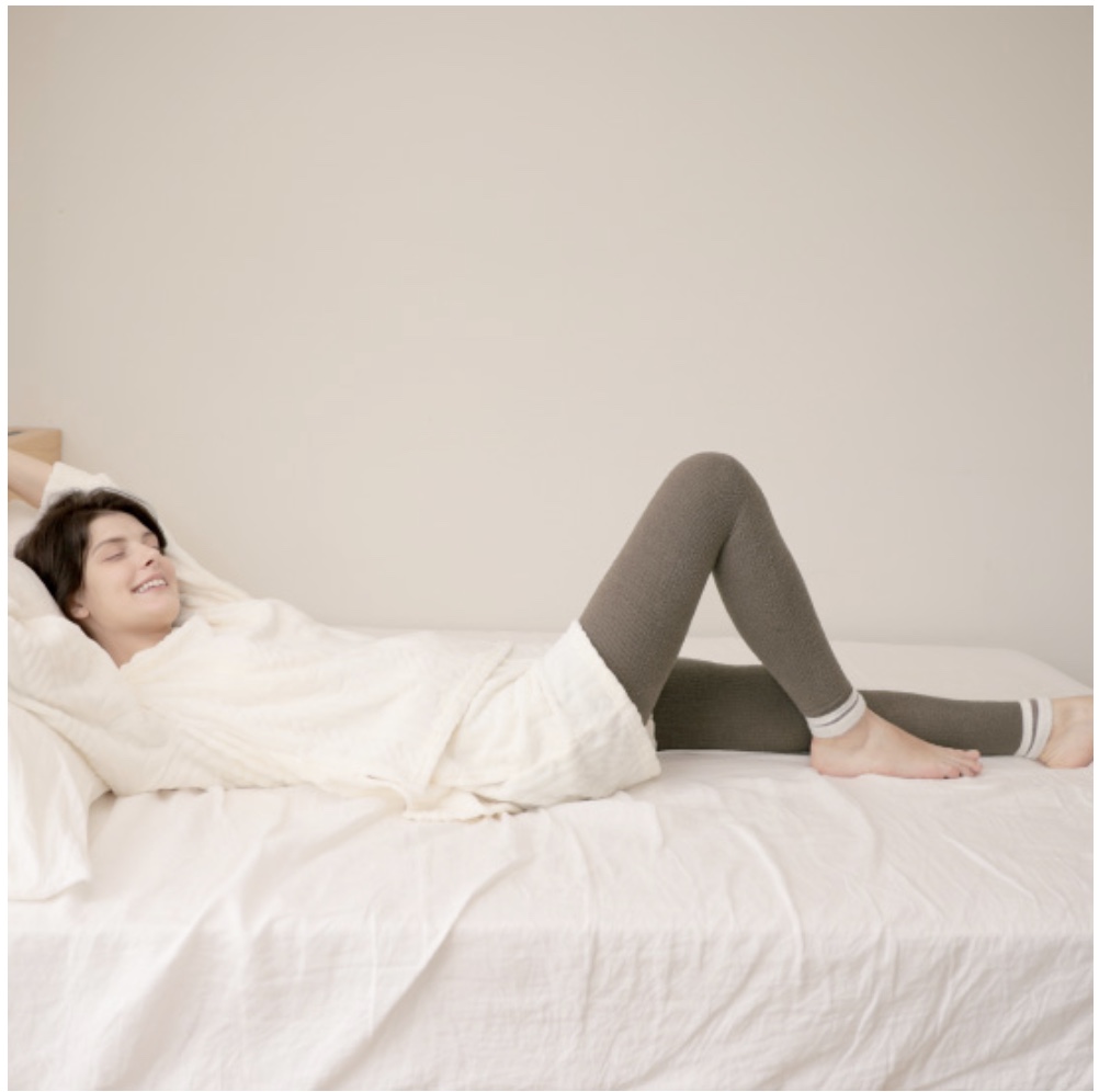 レギンスを履いた楽なルームウェアファッションでベッドに寝転ぶ女性