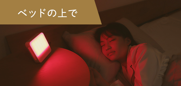 光目覚まし時計の赤色の光を浴びながら、ベッドで眠る女性