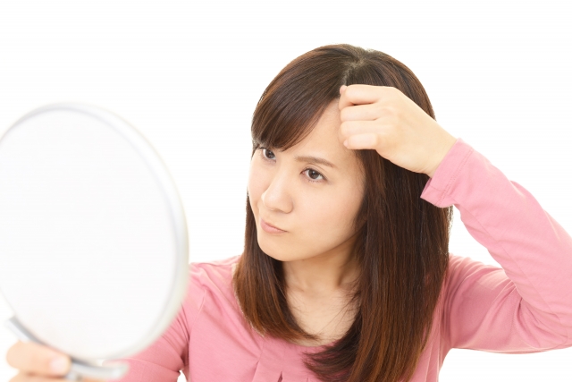 鏡を見ながら、髪の生え際を気にする女性