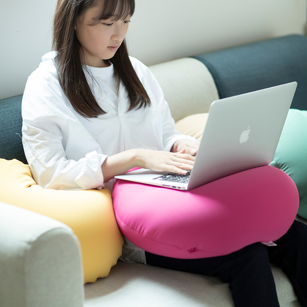 ビーズクッションの上にノートパソコンを乗せて、ソファに座りながら仕事をする女性